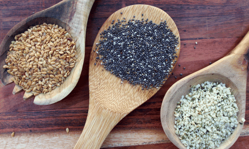 flax, chia and hemp seeds in wooden spoons on a wood table. Healthy fats.