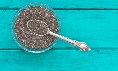 chia seeds in a glass bowl on top of a turquoise wooden table top.