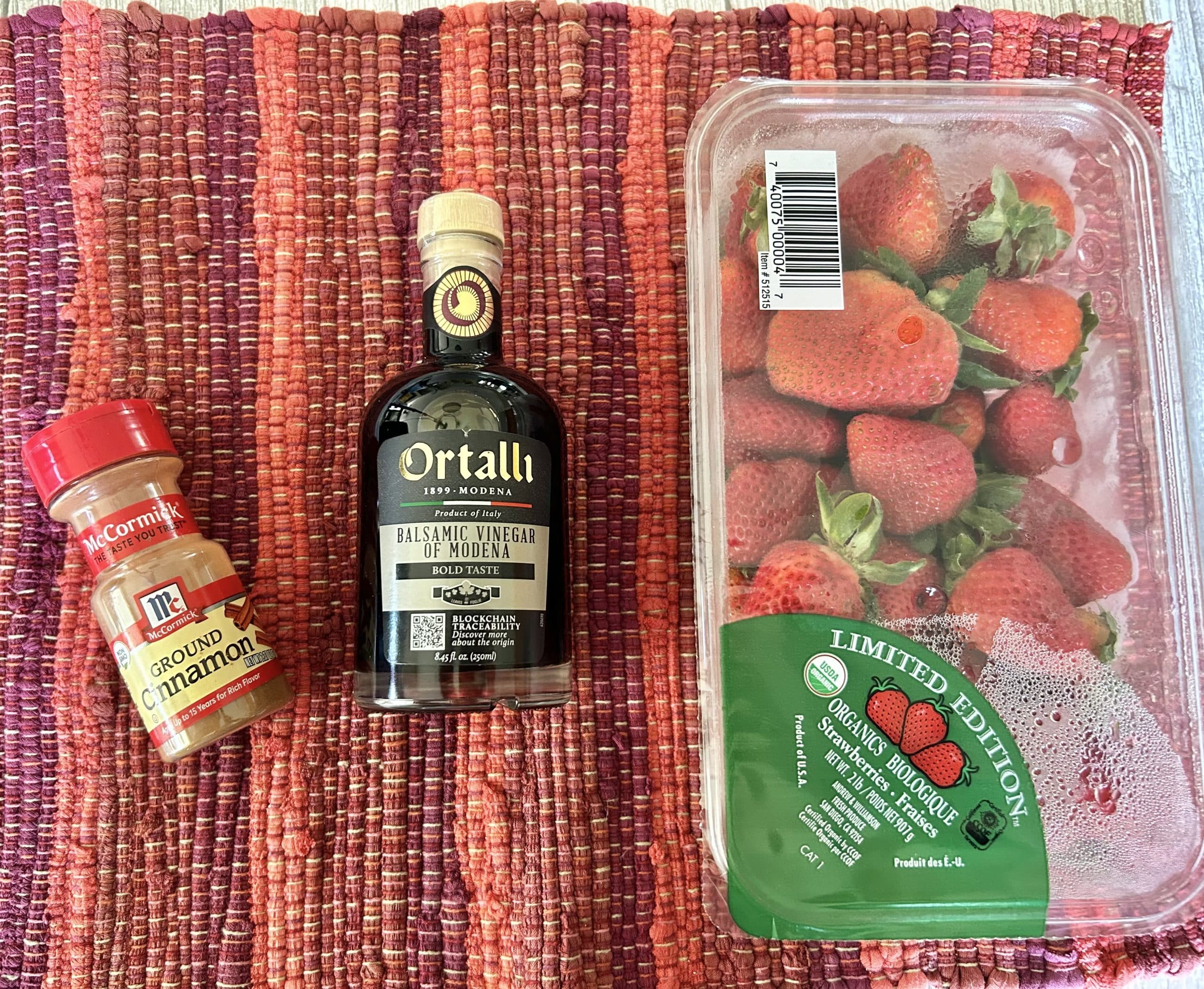 picture of a bottle of ground cinnamon, balsamic vinegar, and a package of strawberries on a red placemat.
