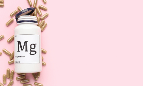 pink background with a bottle of magnesium supplements surrounded by capsules.