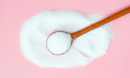 pile of erythritol powder with a wooden spoonful on top of a pink background. Allulose vs erythritol.