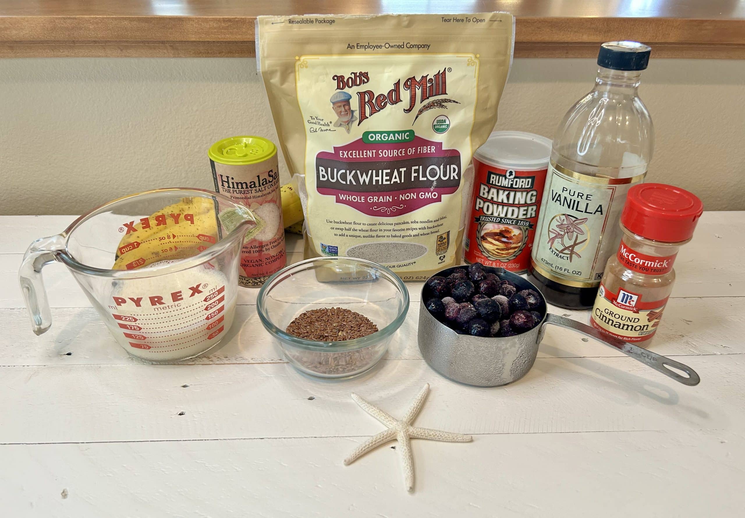 Picture of buckwheat flour, baking powder, vanilla extract, cinnamon, flaxseeds, frozen blueberries, soy milk, Himalayan salt, 2 ripe bananas. Buckwheat Pancakes with blueberries. Veg Out With Maria.