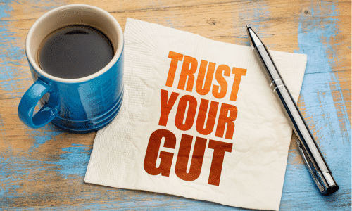 picture of a cup of coffee with a pen and a napkin reading "trust your gut." coffee and gut health.