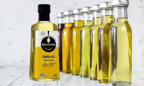 Picture of a bottle of expeller-pressed canola oil in front of a line of other oils. Seed oils